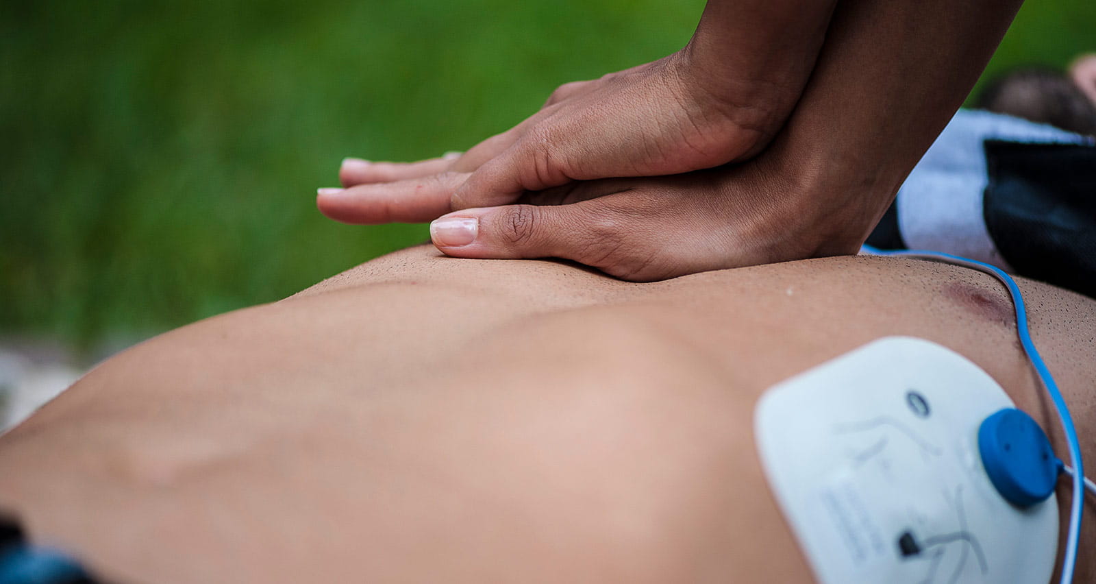A man gives cardiac massage to a fallen man in a park
