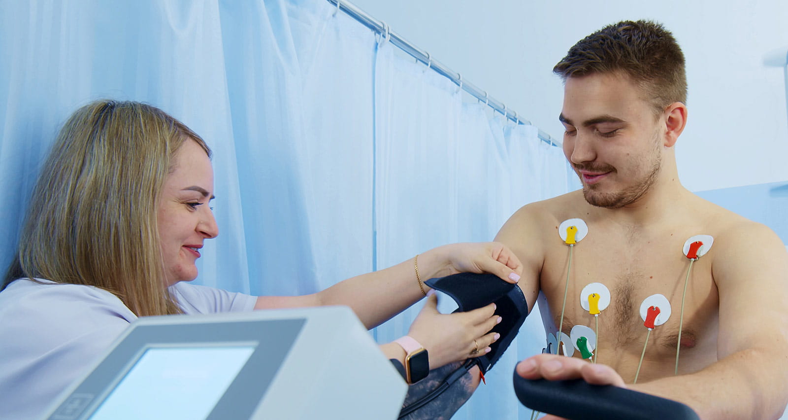 A provider prepares a male patient for an exercise bike ECG test by attaching electrodes to his chest