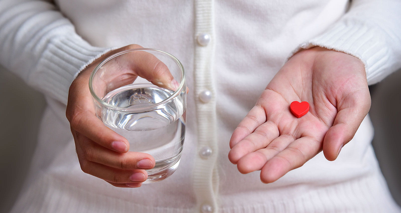 Woman holding a glass of water and a heart-shaped pill
