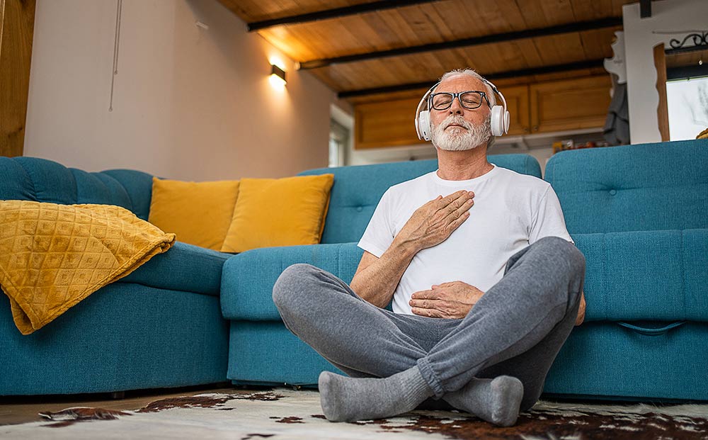 A mature senior man sitting on floor practicing guided meditation at home