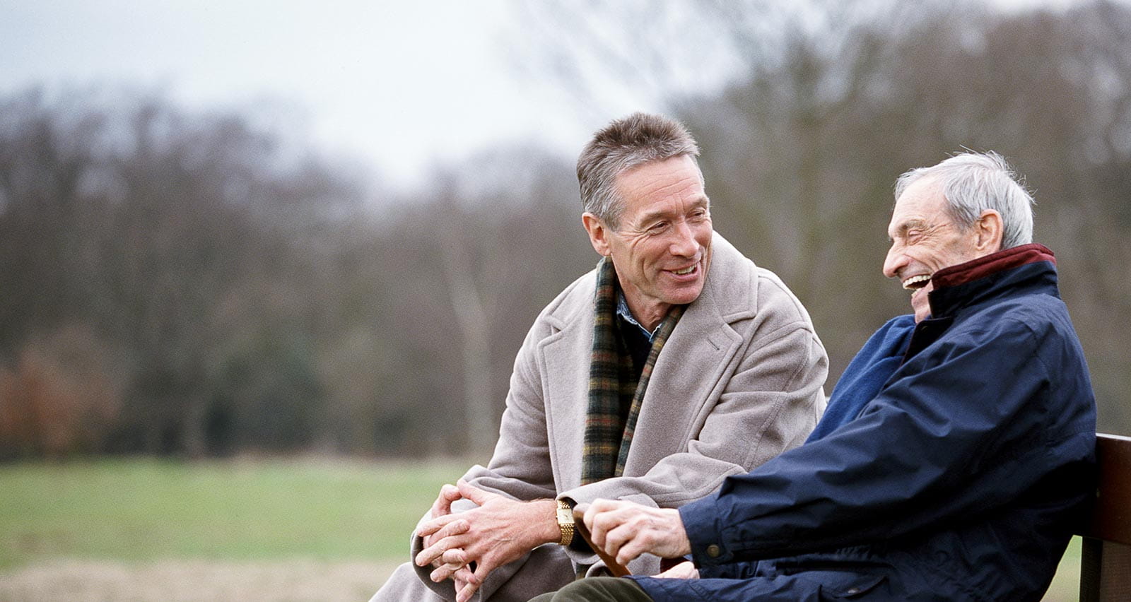 Two older men laughing while sitting on a park bench