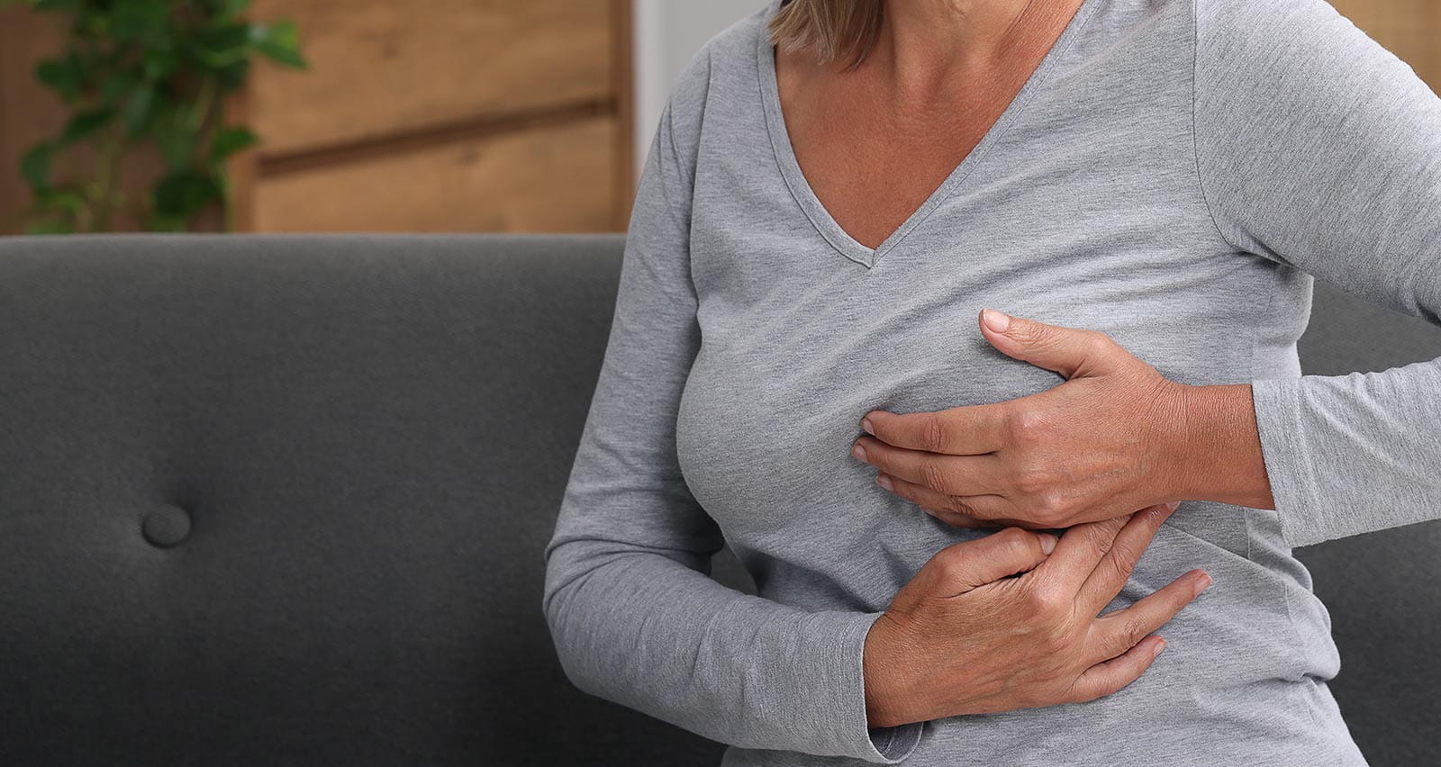 A middle-aged woman examines her breast while sitting on a sofa at home