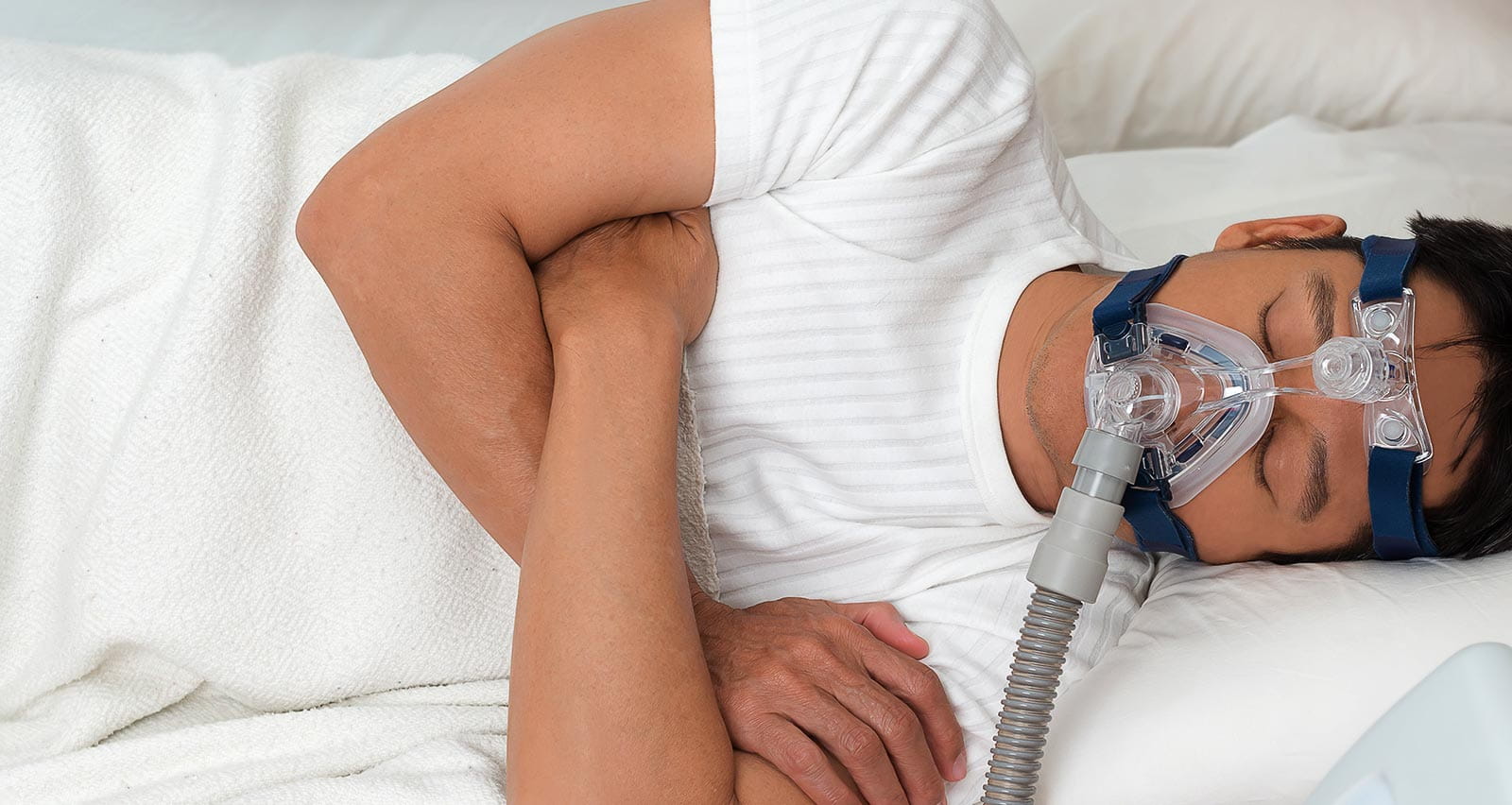 Man in bed wearing CPAP mask for treatment of sleep apnea