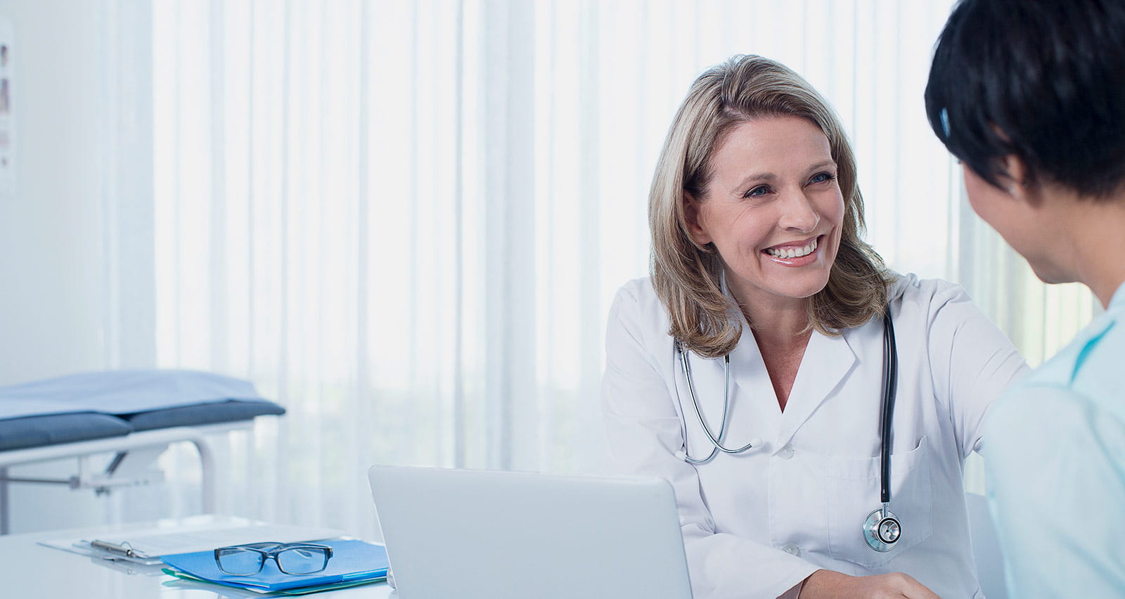 A smiling female doctor and her female patient are sitting at a desk in her office