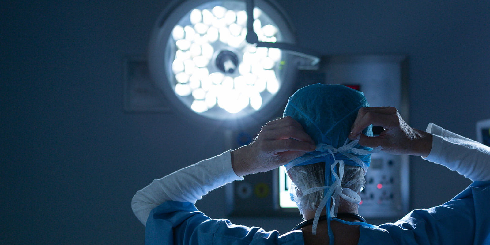 Rear view of female surgeon putting her surgical mask in operating room at hospital